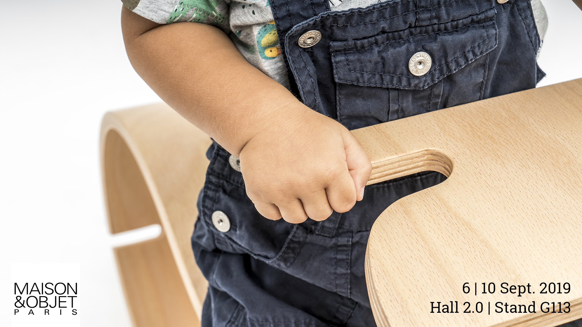 Locandina dell'esposizione del prodotto YaWood di Argo4 presso Maison&Objet a Parigi. Dettaglio della mano di un bambino che afferra del manubrio di YaWood.